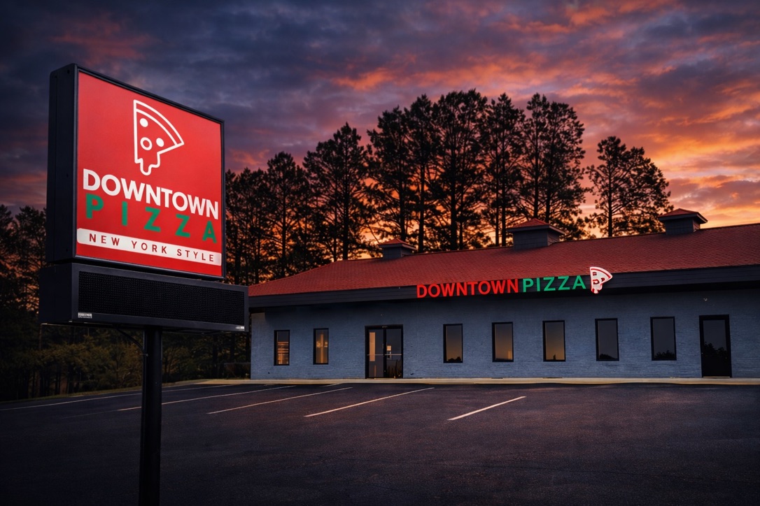 The future Downtown Pizza Inman storefront at 7250 Highway 9 — Highway 9 building with the red pizza-slice marquee sign out front and the DOWNTOWN PIZZA wall sign lit up at sunset.